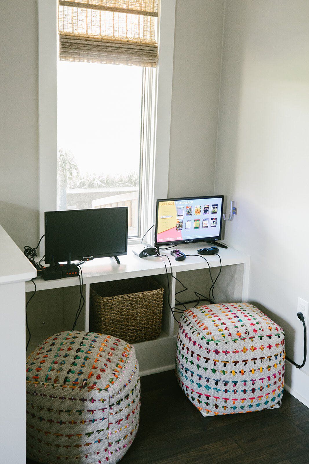There is a desk with a computer on it and two ottomans.