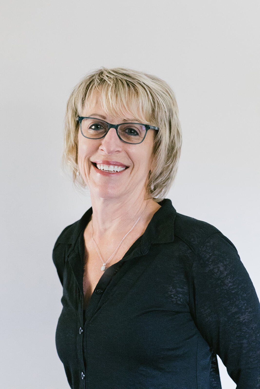 A woman wearing glasses and a black shirt is smiling for the camera.