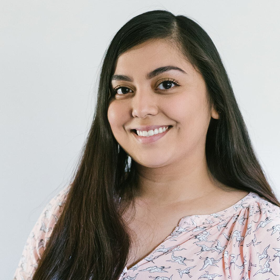 A woman with long hair is smiling for the camera while wearing a pink shirt.