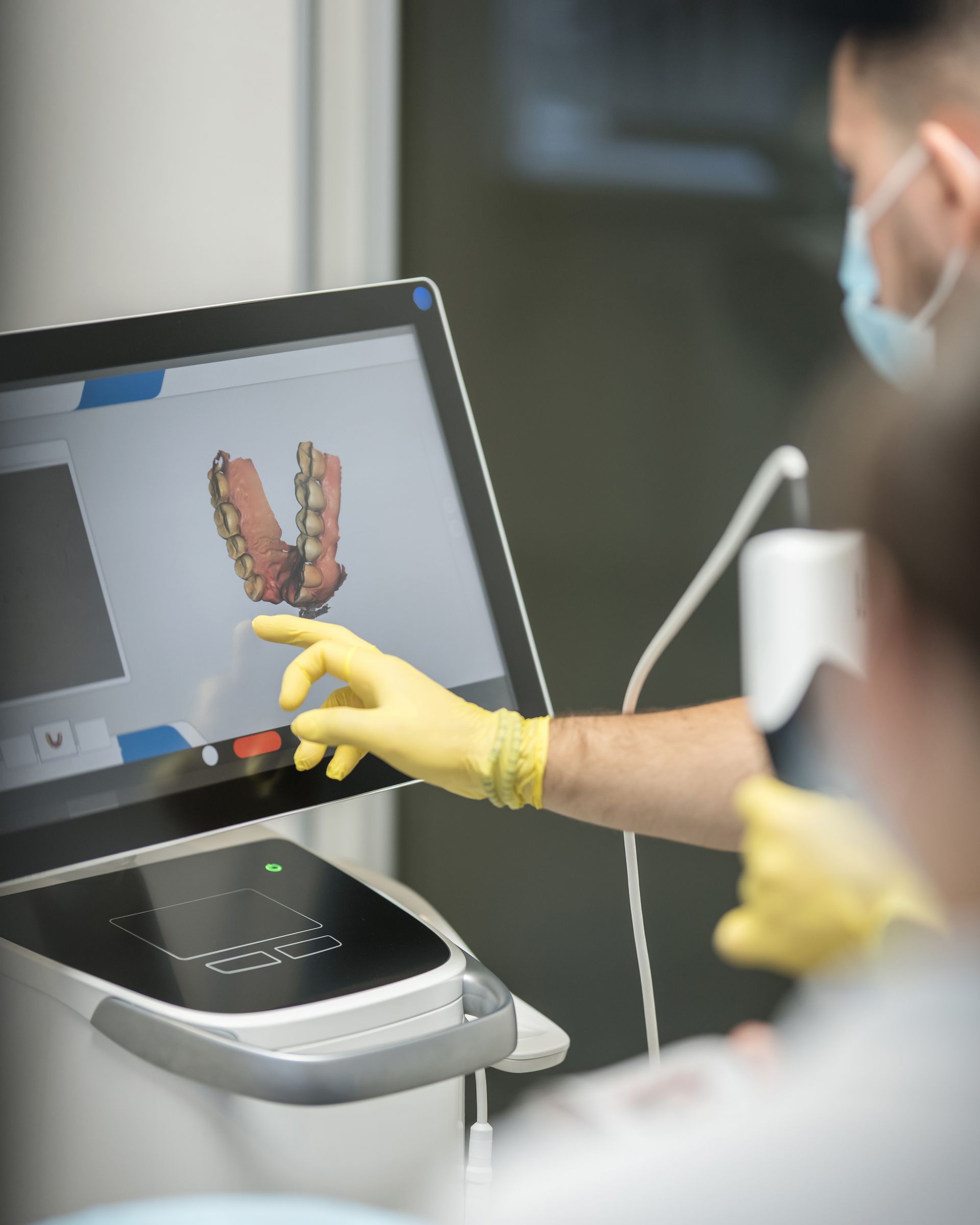 A dentist wearing yellow gloves is pointing at a computer screen