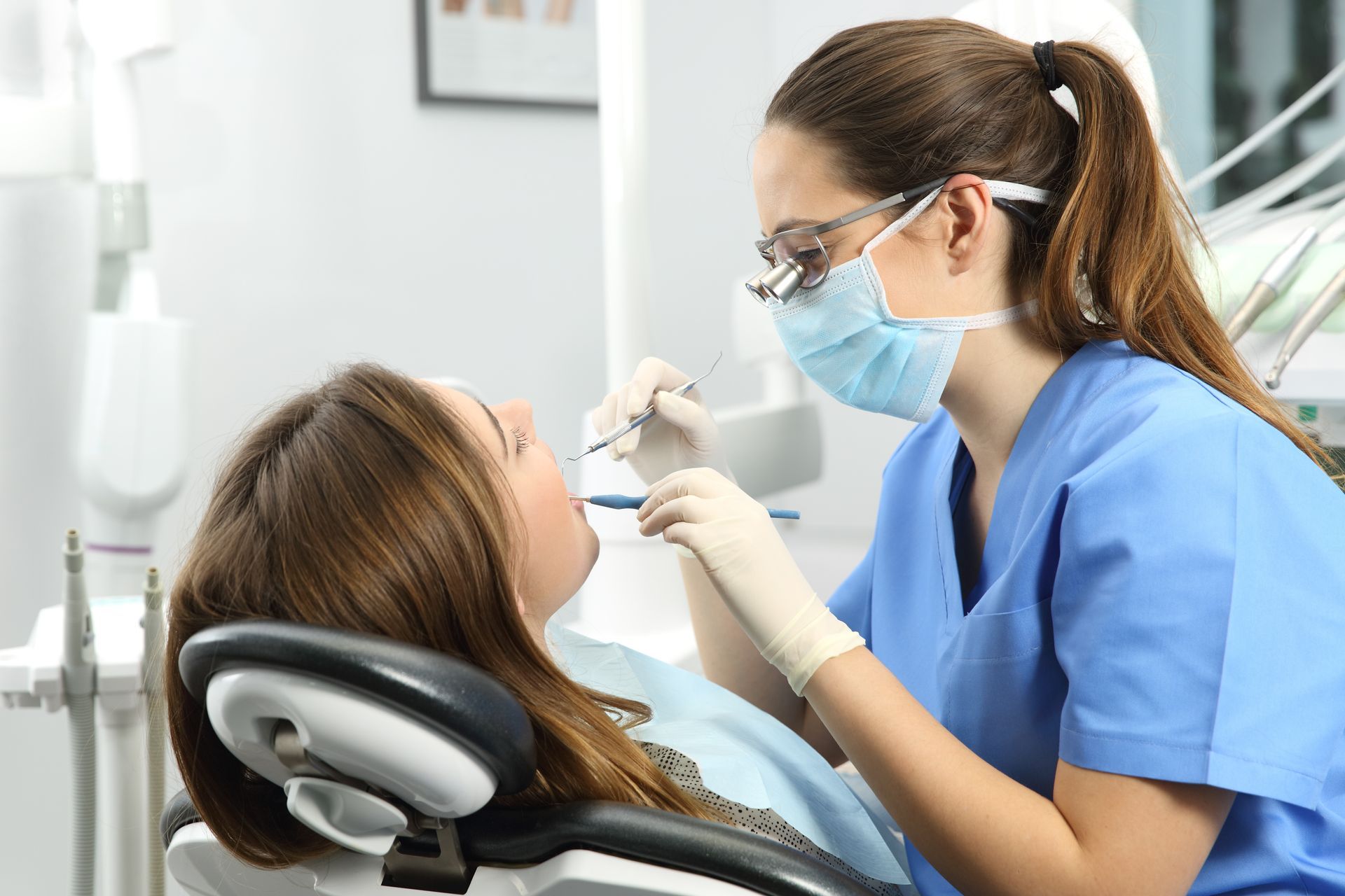 A woman is sitting in a dental chair while a dentist examines her teeth.