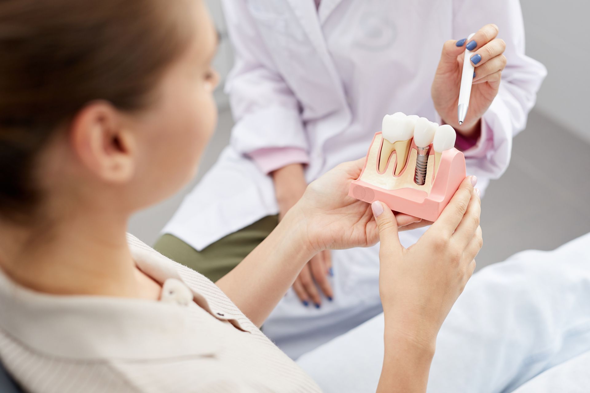 person in dentist office holding a model of a dental implant