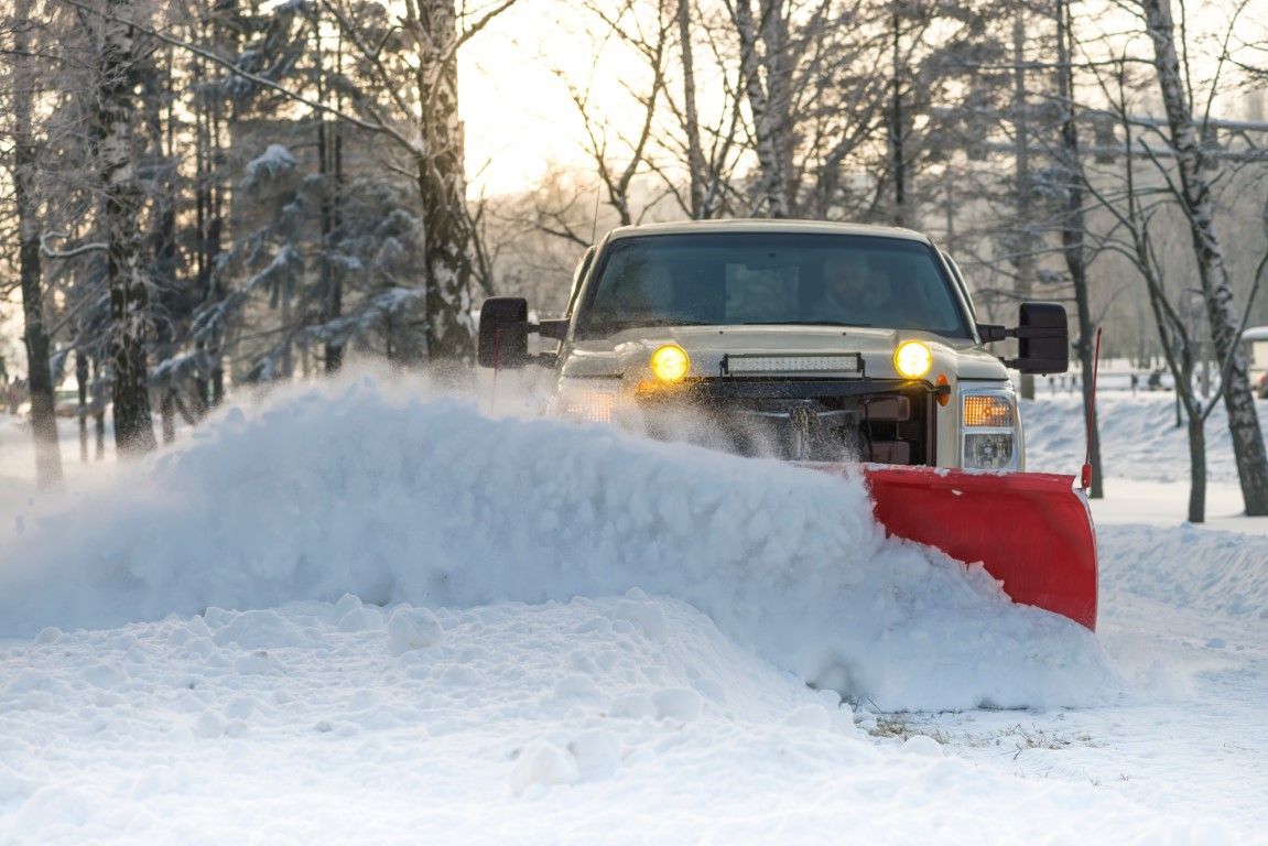 Snow plow clearing snow from a road on a winter day. The truck is white with a red plow.