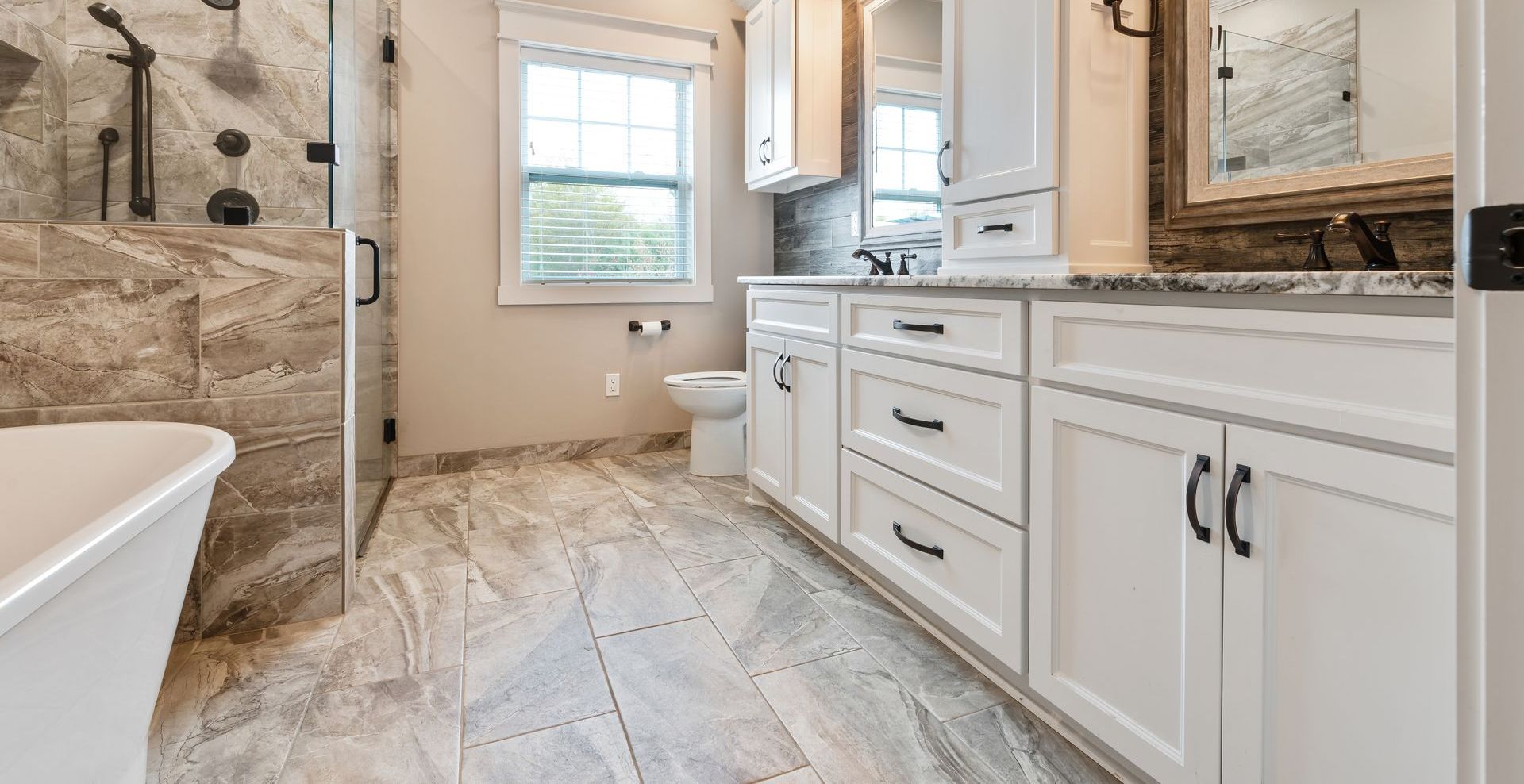 Bathroom with white cabinets, stone floors, and a window.