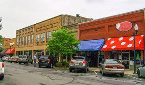 A painting of a small town with cars parked in front of buildings.