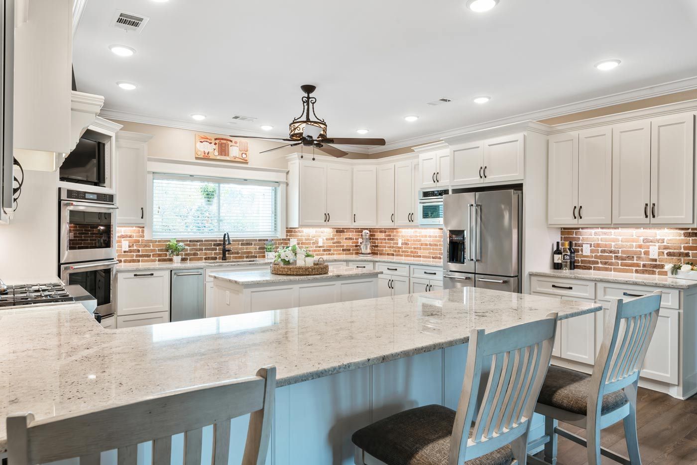 A kitchen with white cabinets , granite counter tops , stainless steel appliances and a large island.