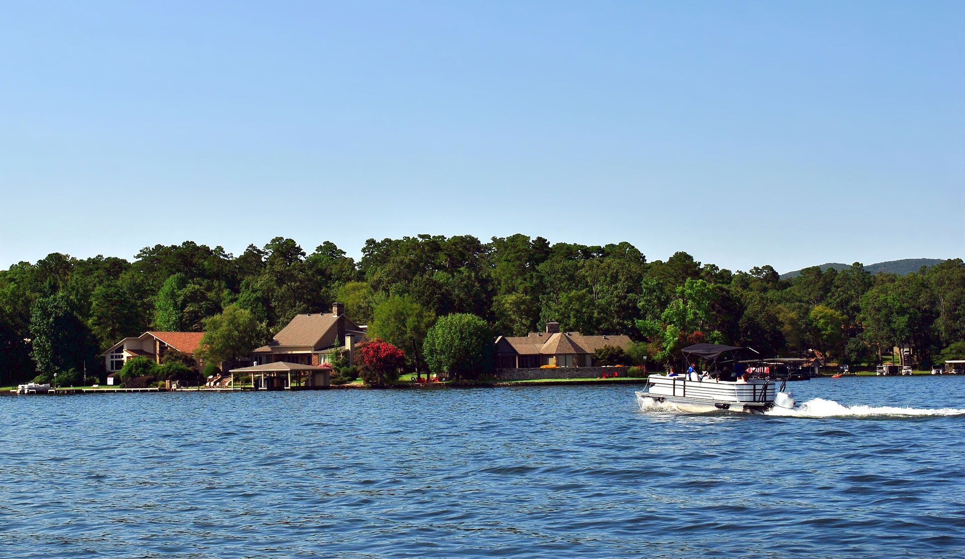 A boat is floating on a lake with houses in the background.