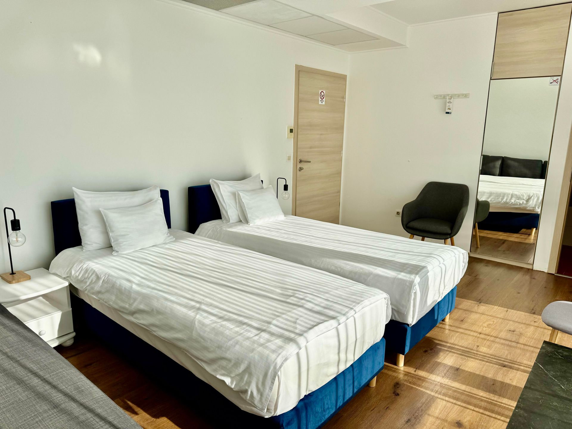 A hotel room with two beds , a chair and a mirror.