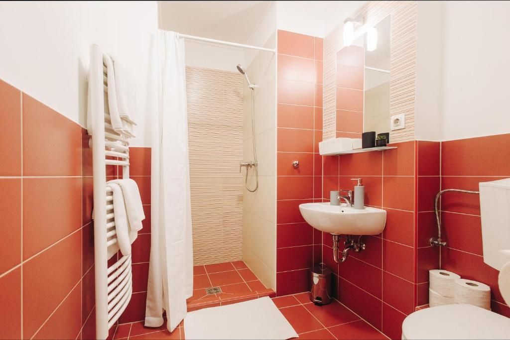 A bathroom with red tiles , a sink , toilet and shower.