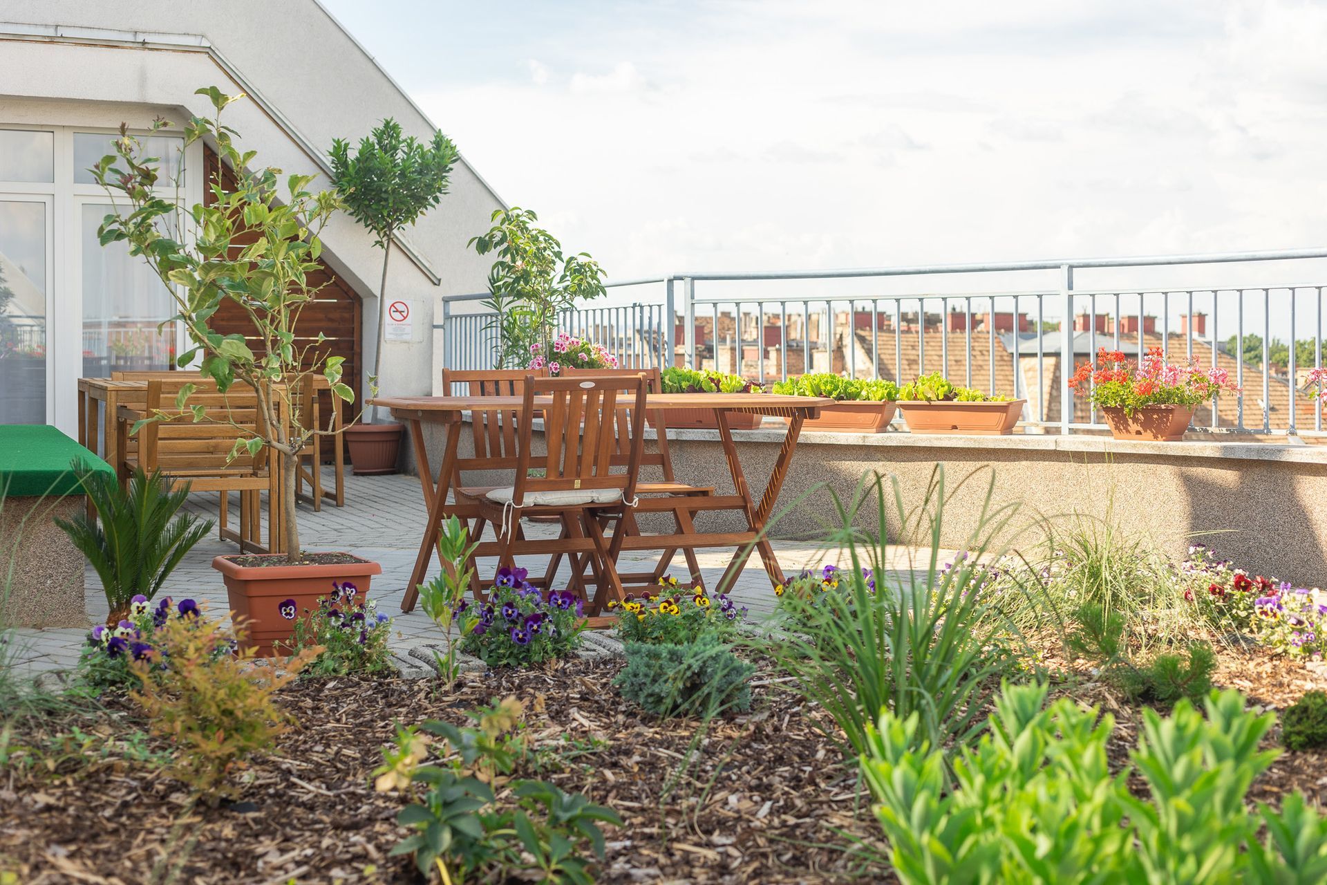 A rooftop garden with a table and chairs surrounded by potted plants.