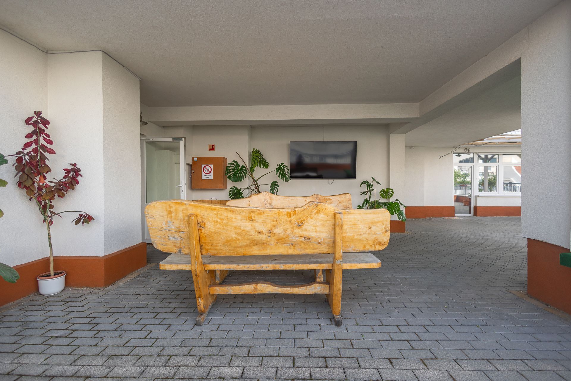A wooden bench is sitting in a brick courtyard next to a television.