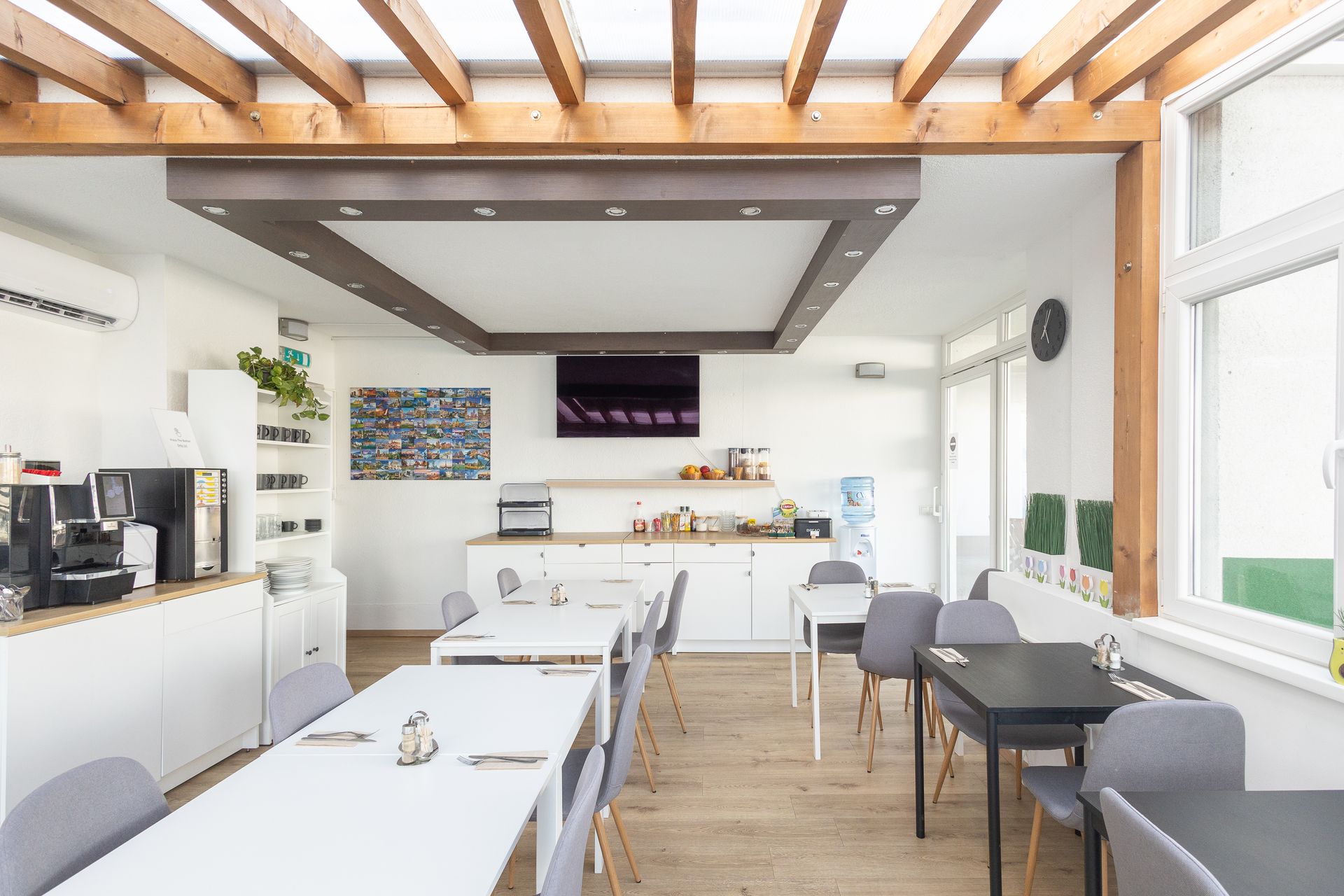 A large room with tables and chairs and a television on the ceiling.
