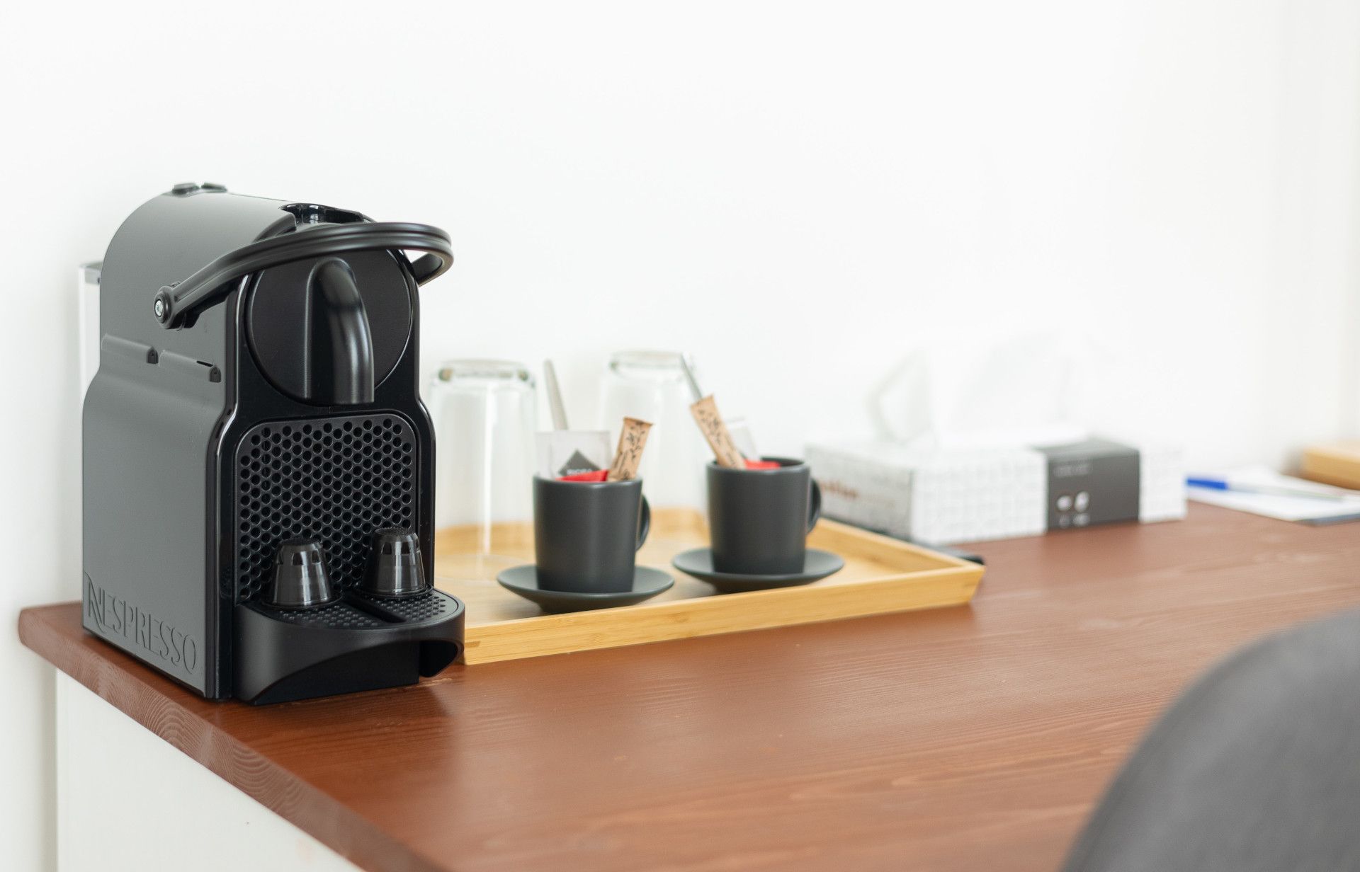 A coffee machine is sitting on a wooden table next to a tray of cups and saucers.