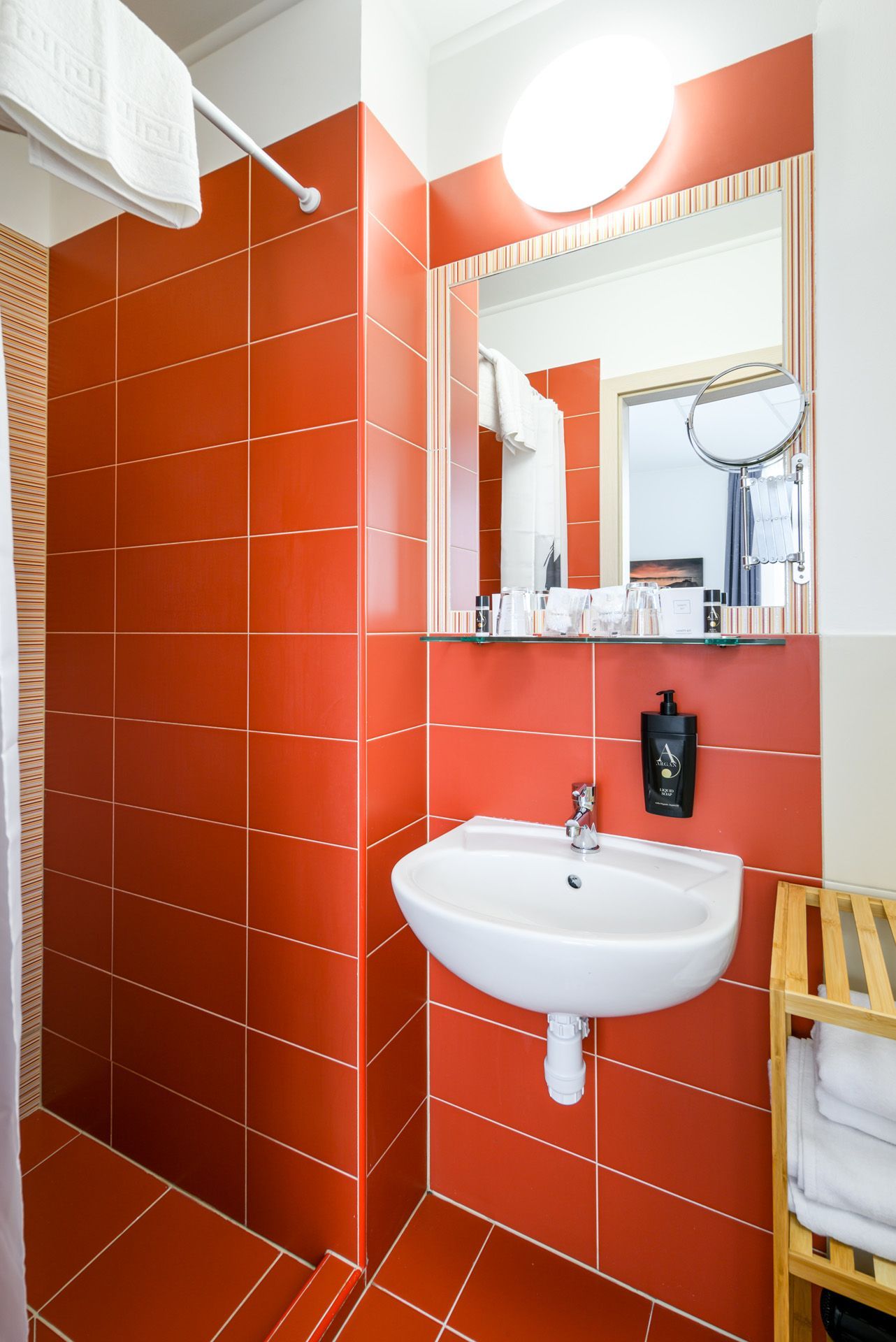 A bathroom with red tiles and a sink and mirror