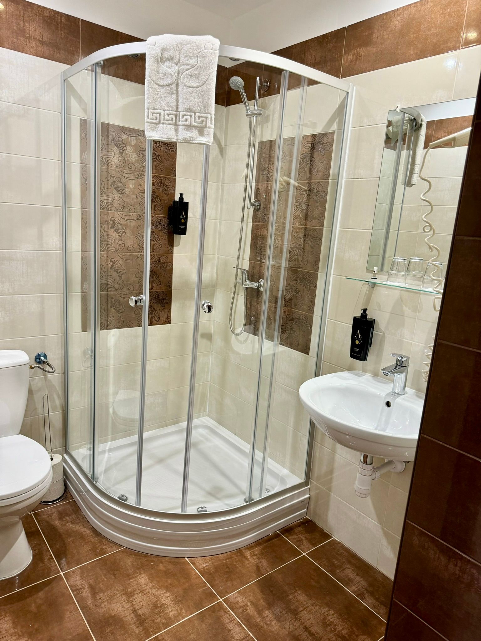 A bathroom with a shower , sink , toilet and mirror.