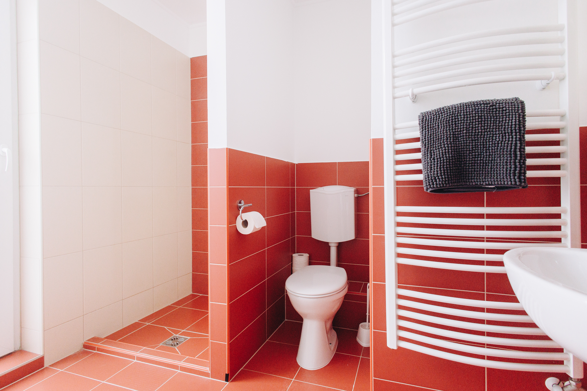 A bathroom with red tiles , a toilet , a sink and a towel rack.