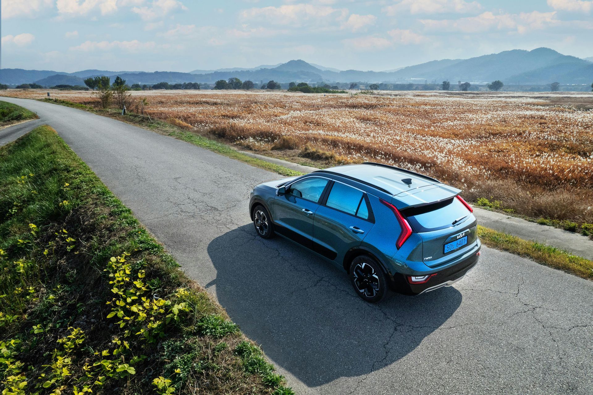 Blue SUV on a narrow road in a rural setting, with fields and mountains in the background.