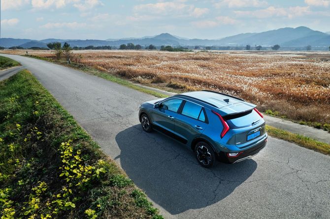 A blue car is driving down a road next to a field.