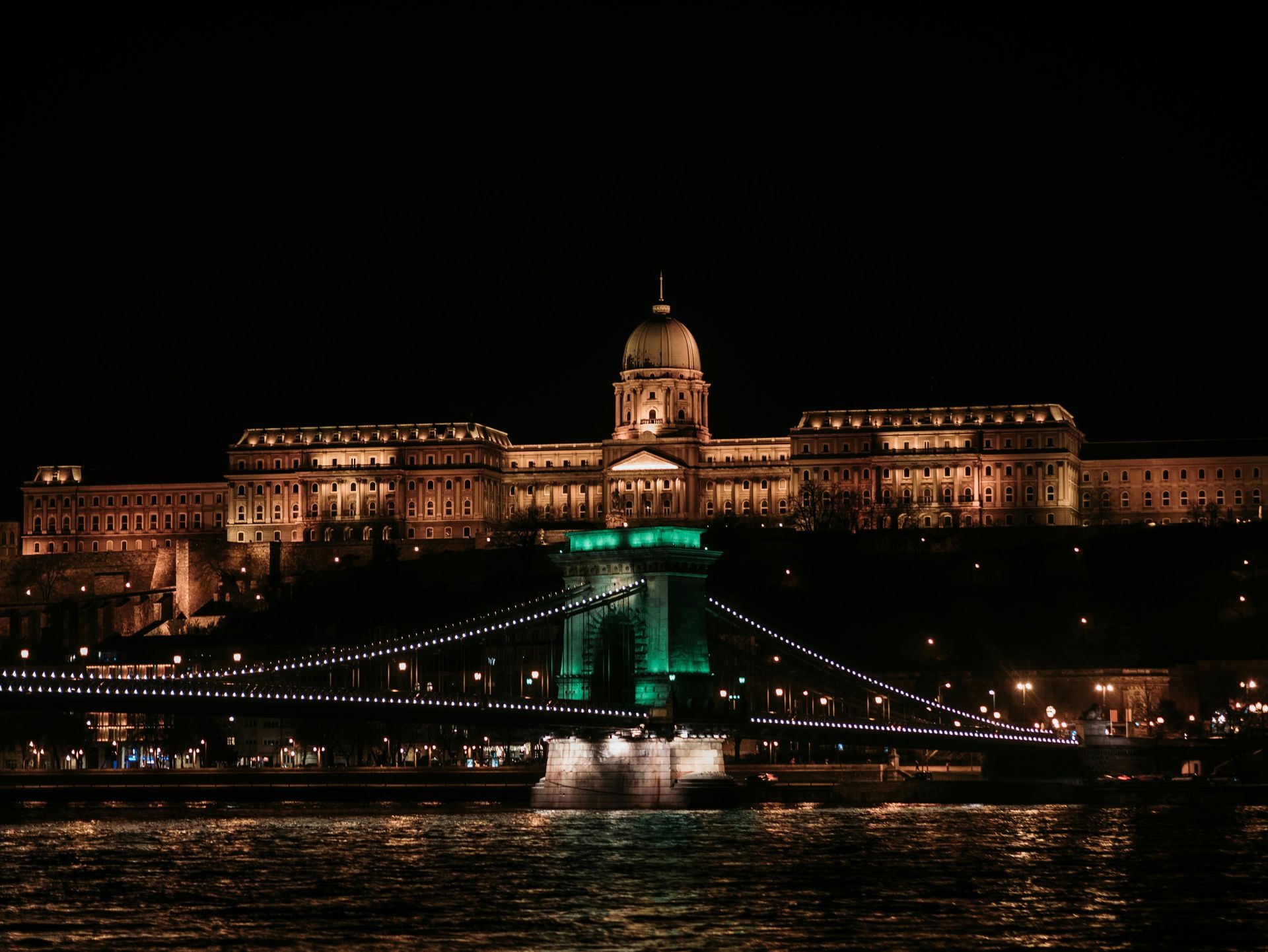 A cityscape at night with a castle in the foreground and a crane in the background.