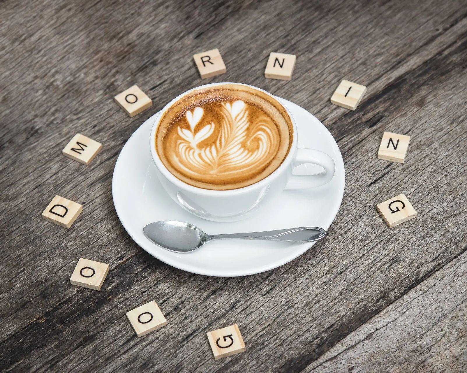 Latte in a white cup on saucer with spoon, surrounded by wooden blocks spelling 