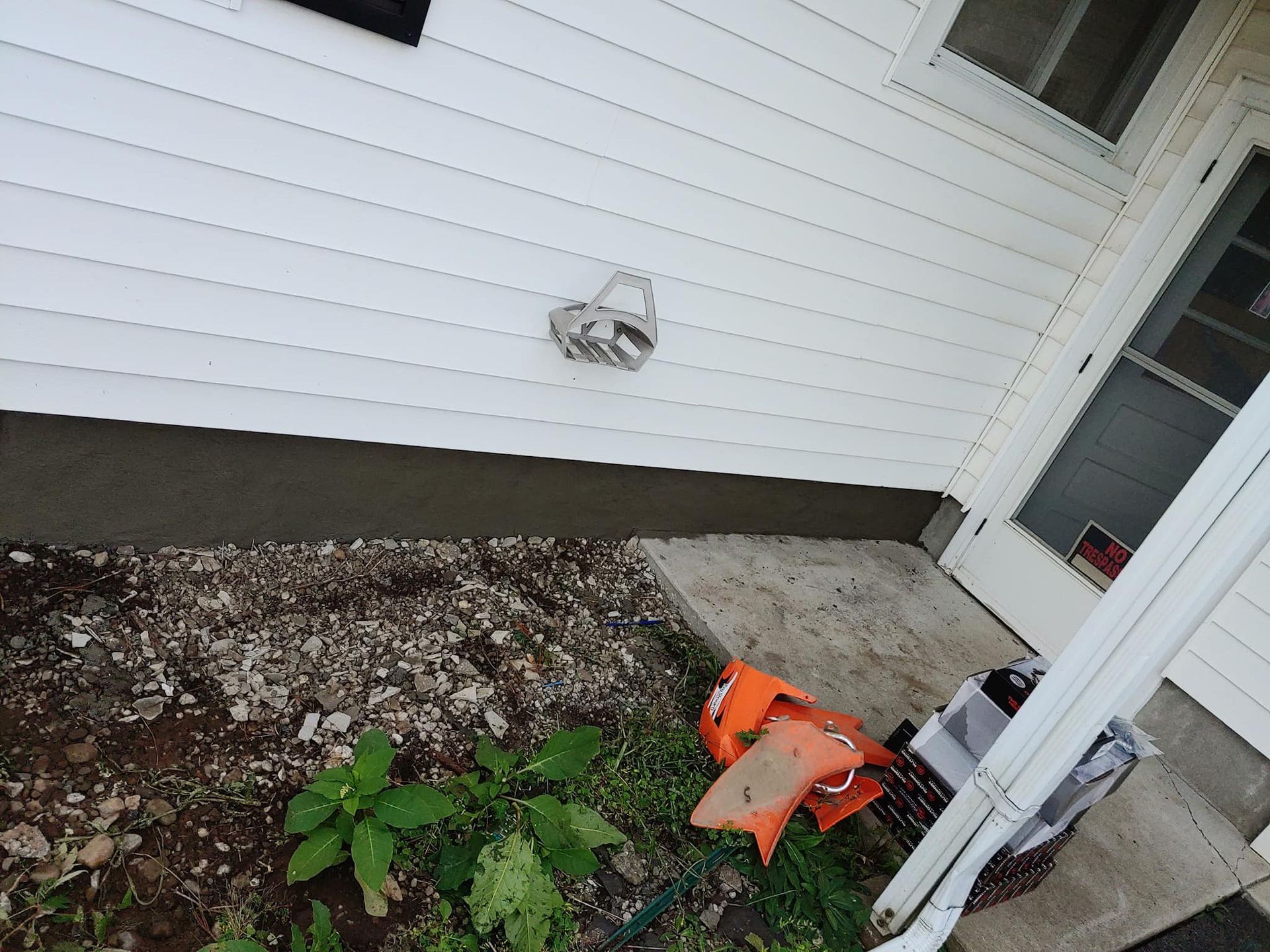 White house exterior with vent, concrete, ground cover, door, and plants.