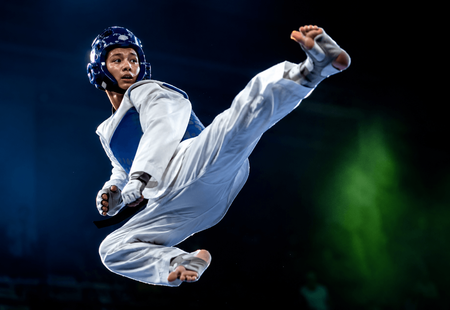 HWCTA Martial artist in white uniform and blue helmet performing a high flying kick on a dark stage with green light.