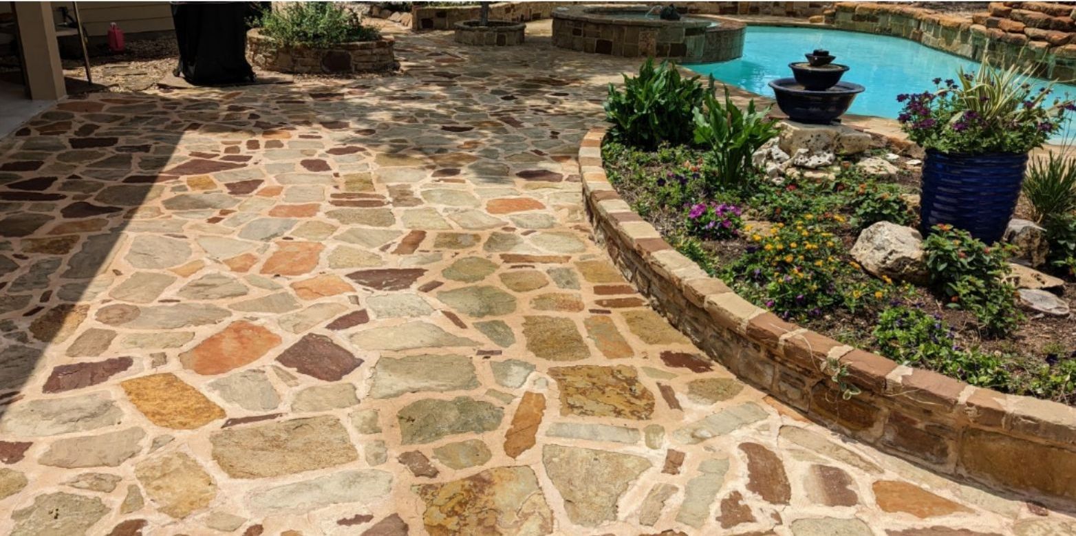 A stone walkway leading to a pool next to a garden.