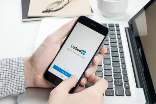 A person is holding a cell phone in front of a laptop.