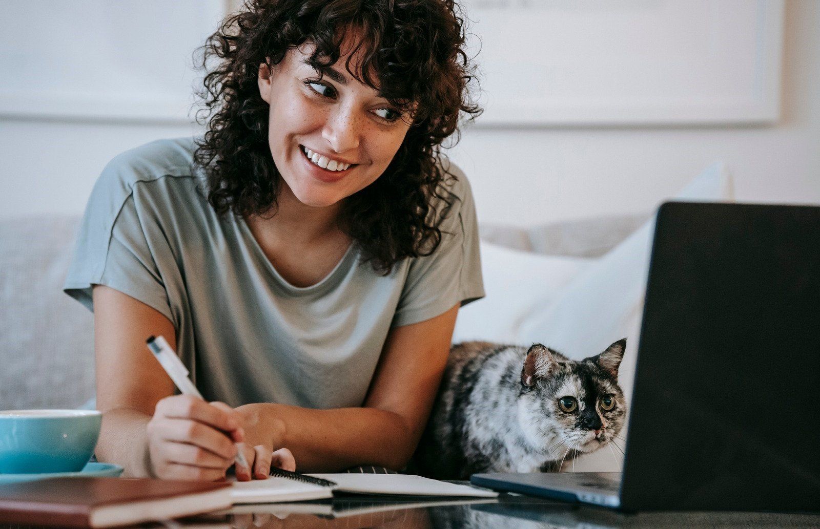 A woman is sitting at a table with a laptop and a cat.