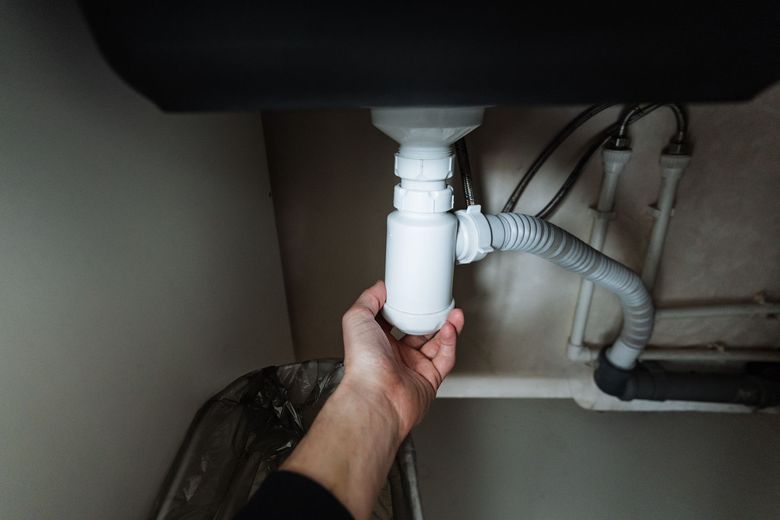 Hand unscrewing a white plastic P-trap under a black sink, in a domestic setting.