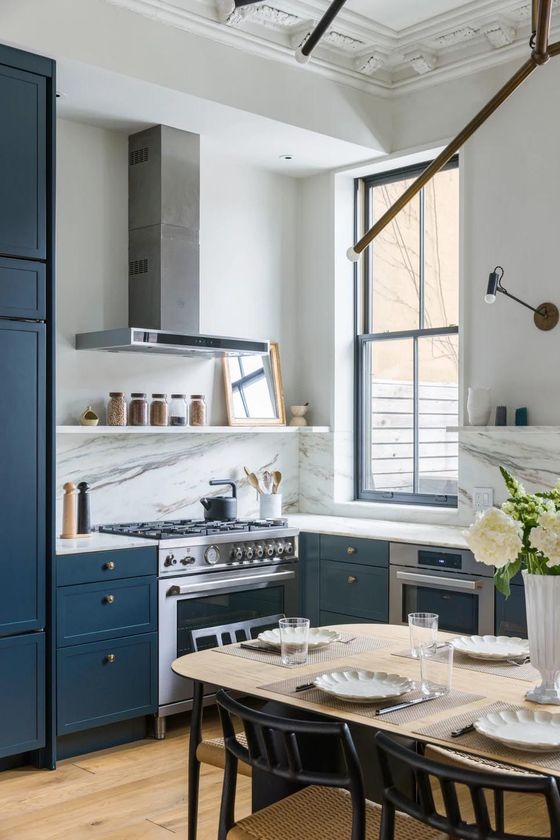 A kitchen with blue cabinets , a stove , a table and chairs.