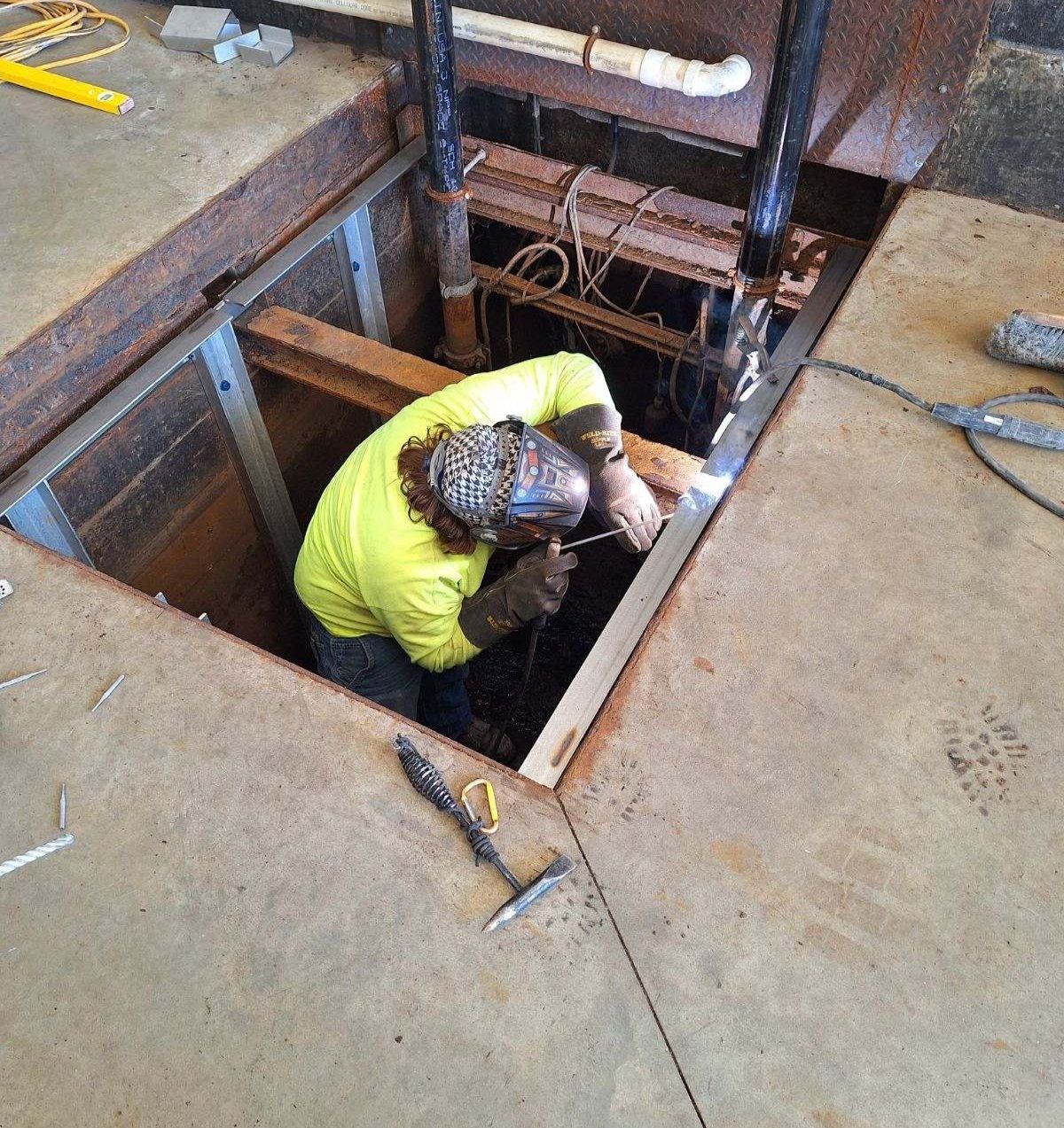 A man in a yellow shirt is welding in a hole