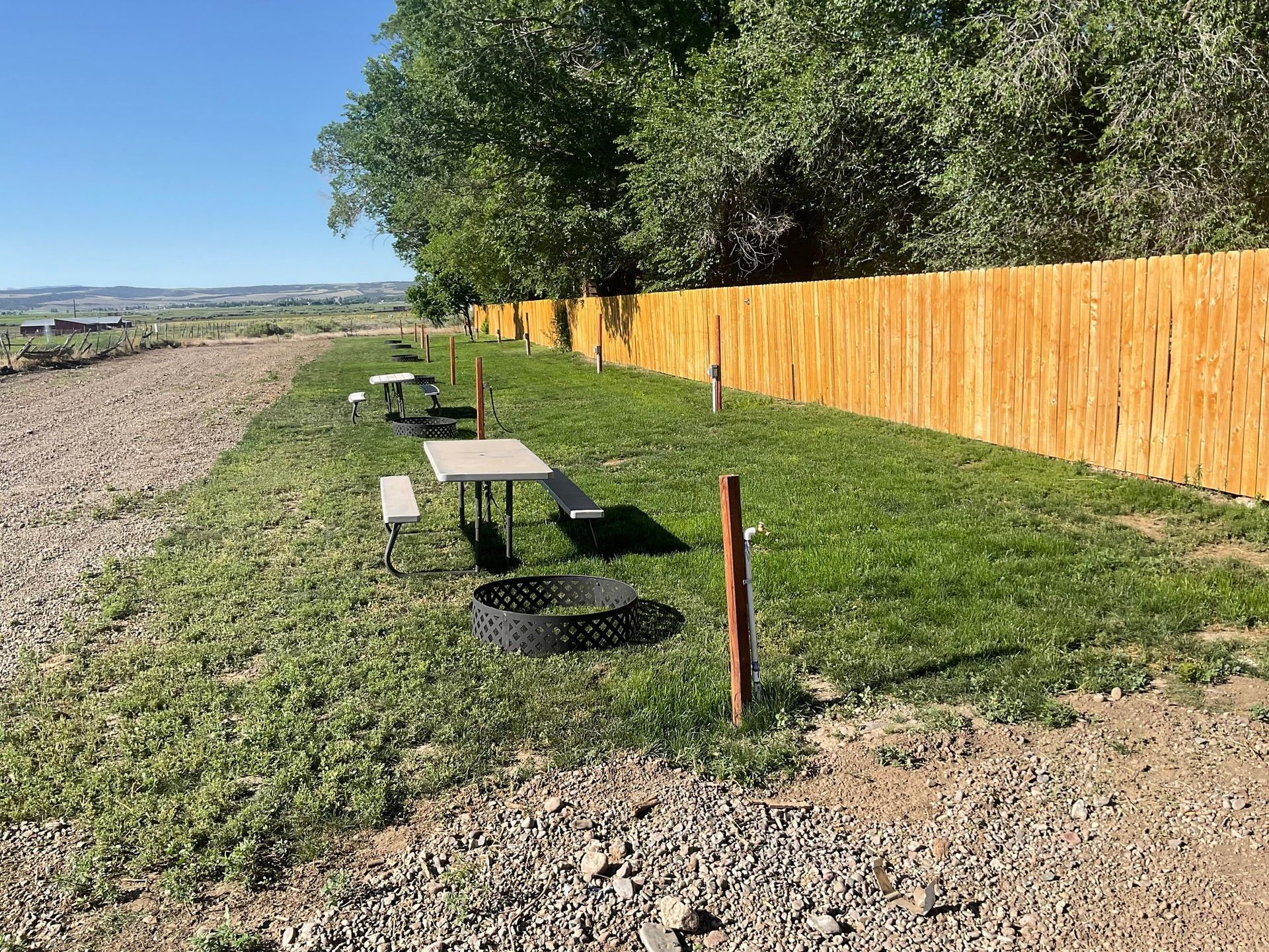A picnic table and benches are sitting in the grass next to a wooden fence.