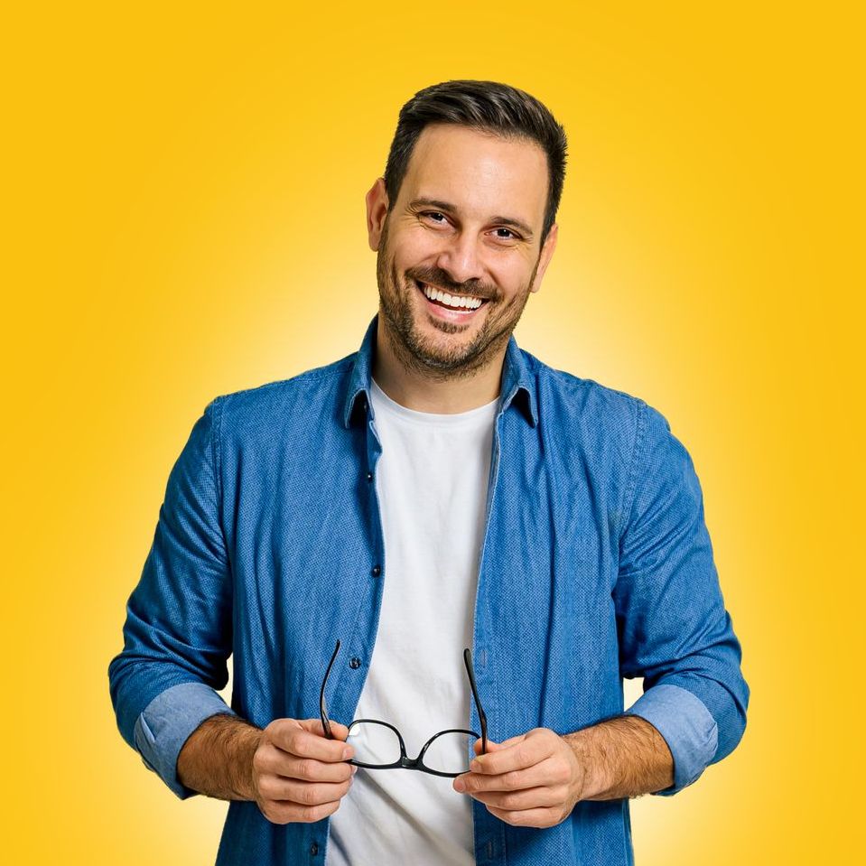 A man in a blue shirt is holding a pair of glasses and smiling.