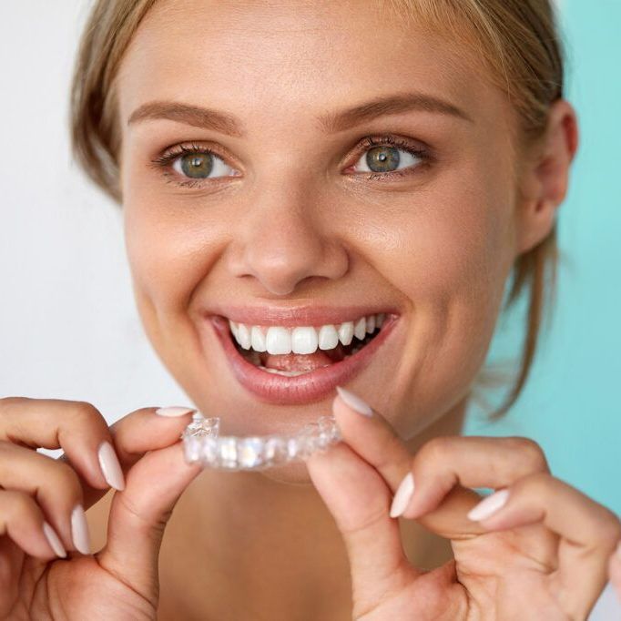 A woman is smiling while holding a clear retainer in front of her teeth