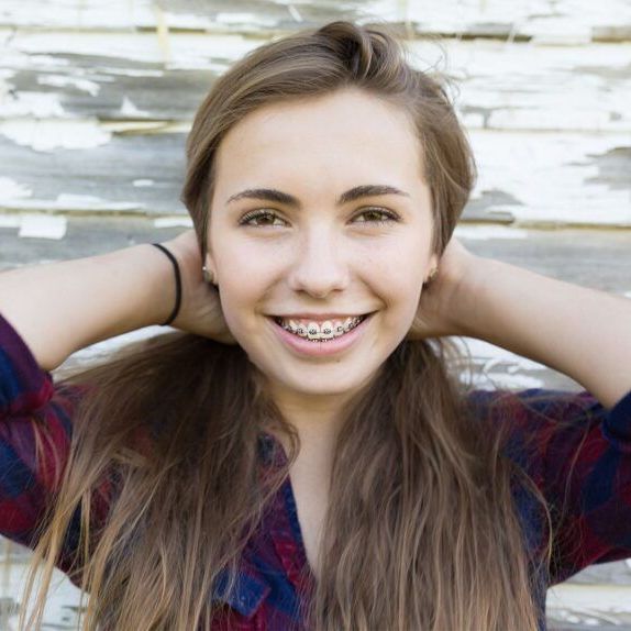 A woman with braces on her teeth is smiling with her hands behind her head