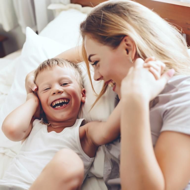 A woman and a child are laying on a bed and smiling.