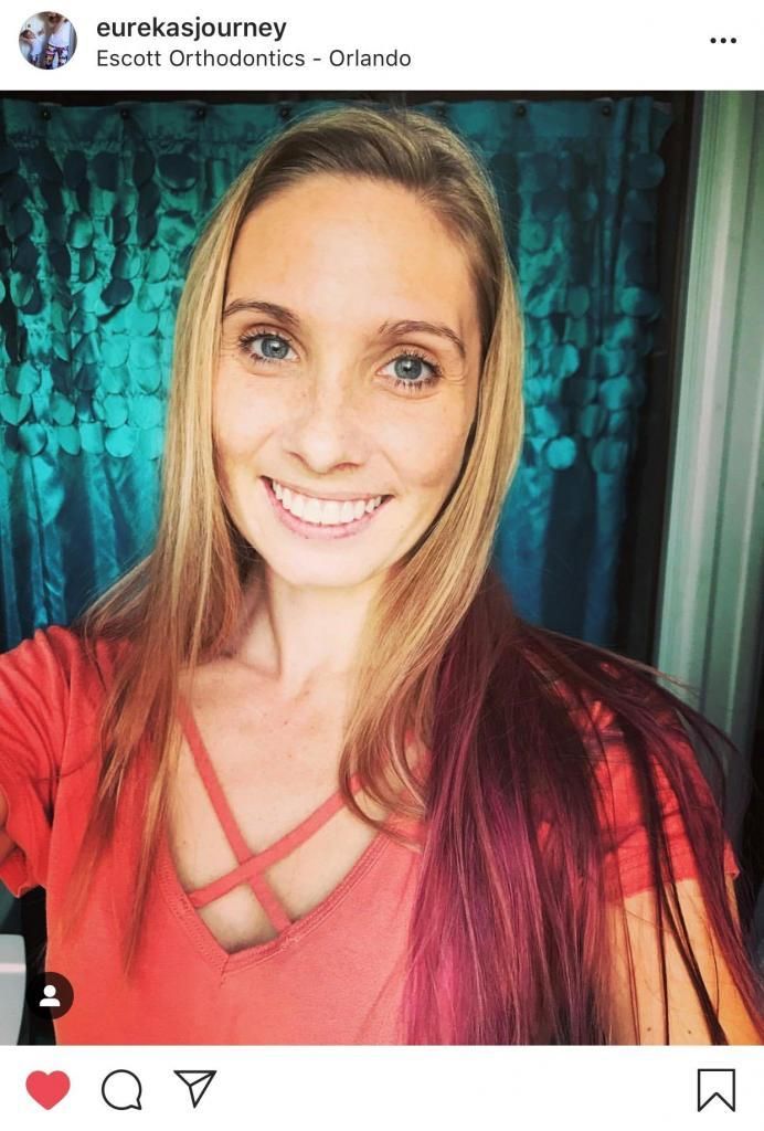 A woman in a red shirt is smiling and taking a selfie.