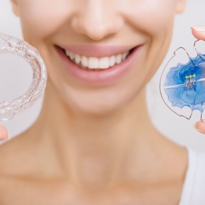 A woman is smiling while holding a retainer in front of her teeth.