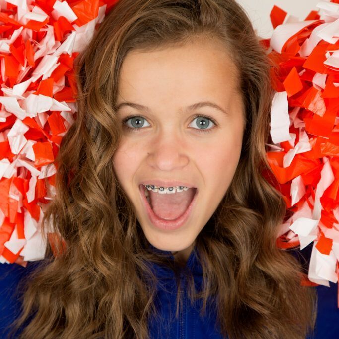 A girl with braces on her teeth is surrounded by orange and white pom poms