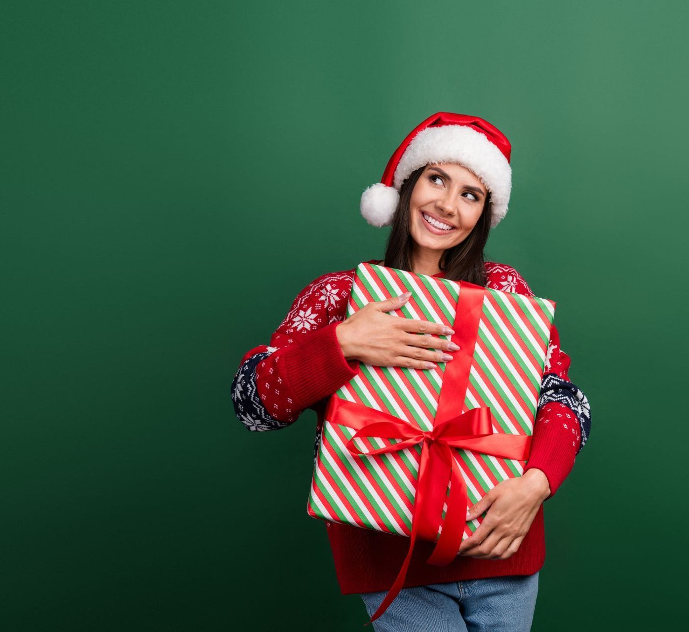 A woman in a santa hat is holding a striped christmas present.