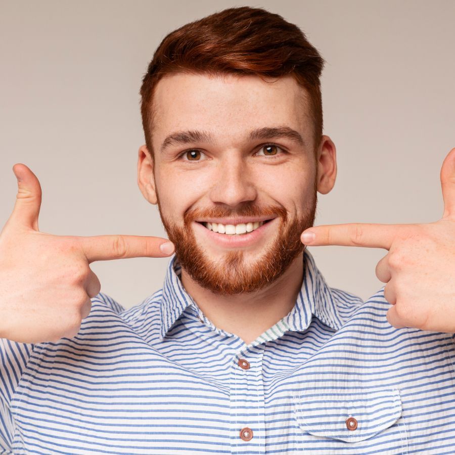 A man with a beard is pointing at his teeth and smiling.