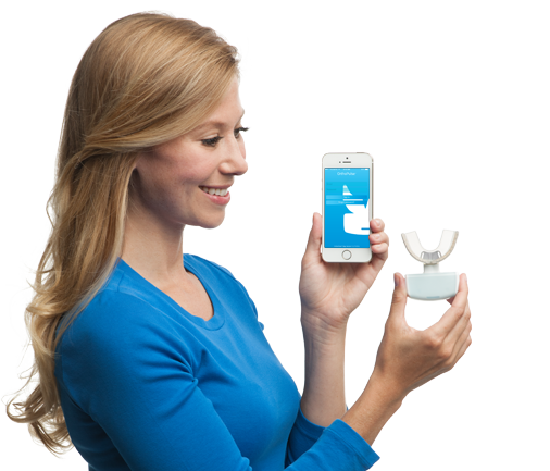 A woman in a blue shirt is holding a phone and a toothbrush