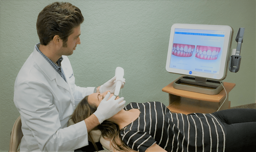 A dentist is examining a woman 's teeth in front of a computer screen.