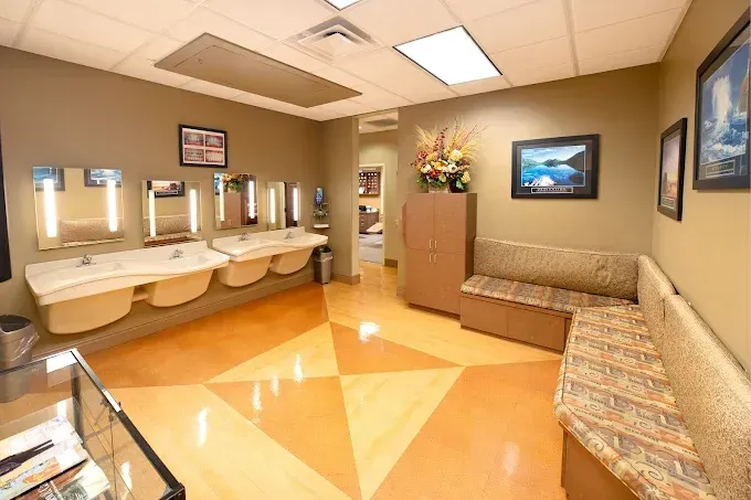 Waiting room with sinks, seating, floral arrangement, and framed artwork.