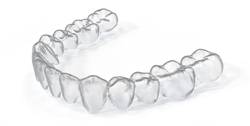 A transparent plastic dental aligner for the lower teeth against a white background.