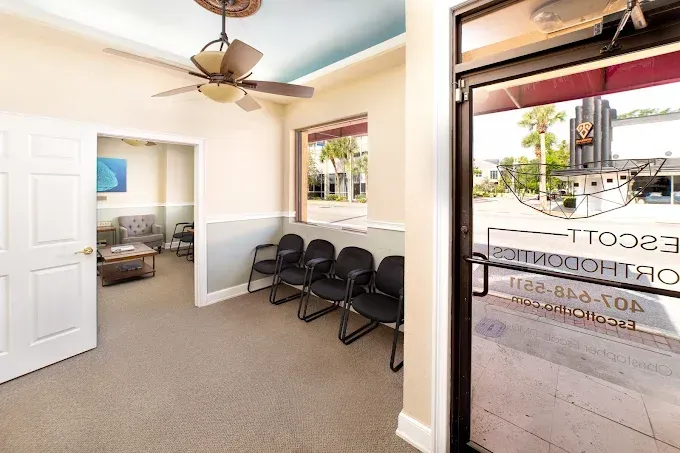 Waiting room with chairs, door, window, and view of the outside. Ceiling fan, tan walls, and a door to another room.