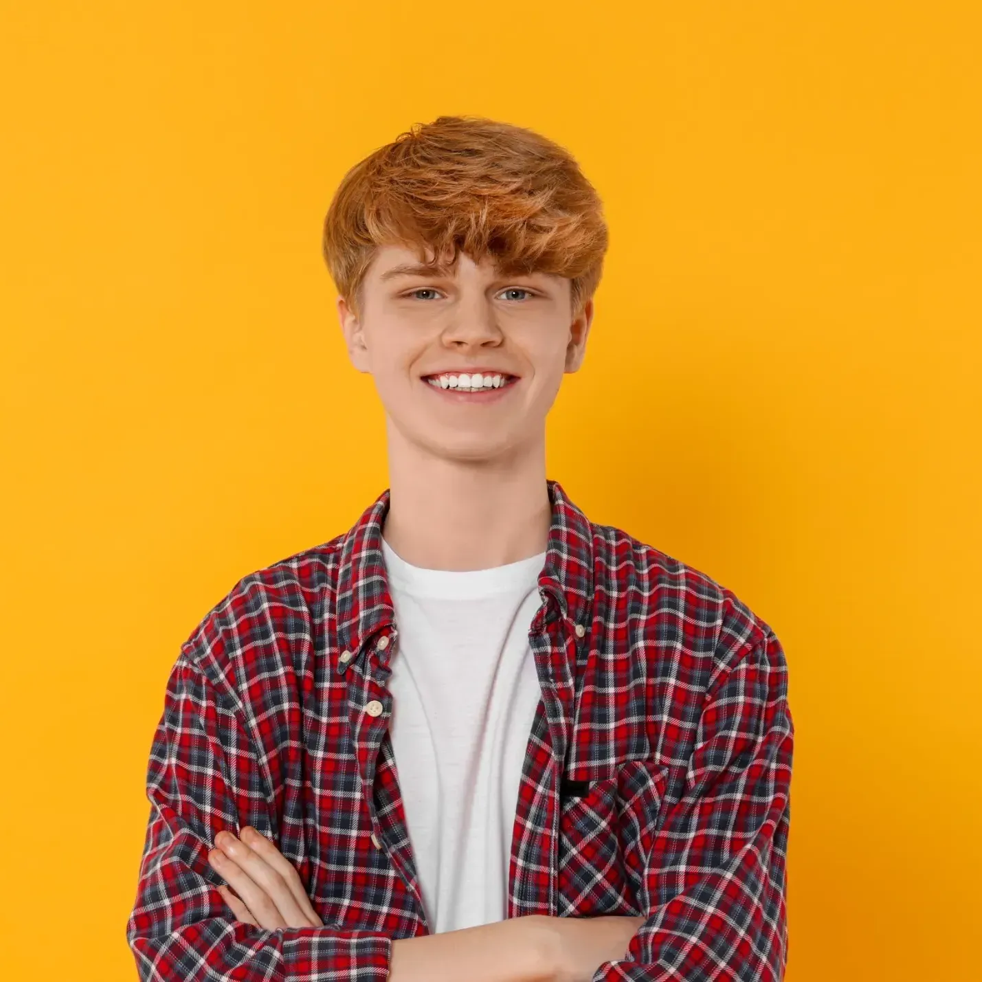 A young man in a plaid shirt is smiling with his arms crossed.