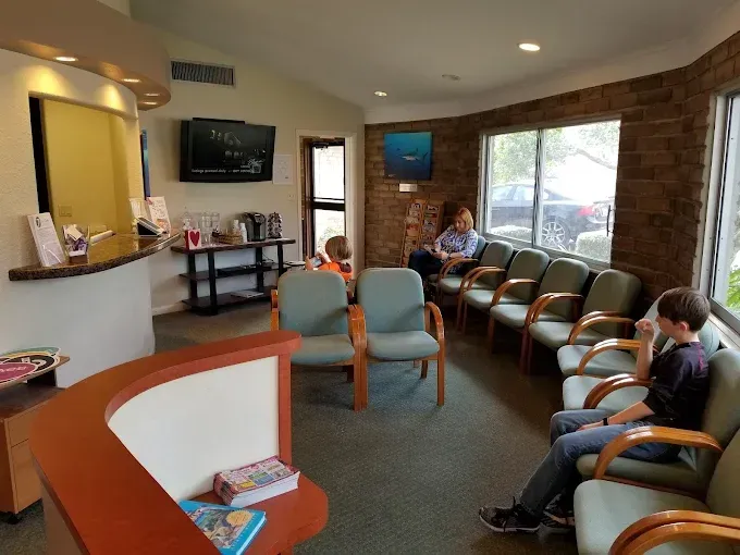 Waiting room with chairs, TV, and reception desk. People are seated.