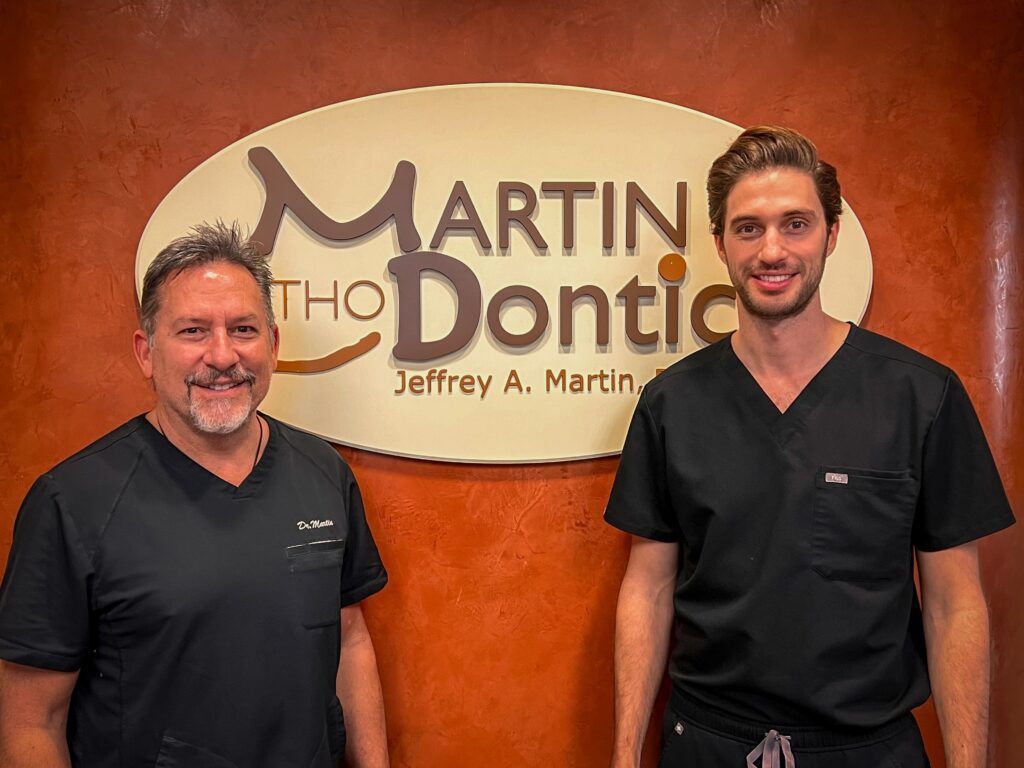 Two men in scrubs are standing in front of a sign.